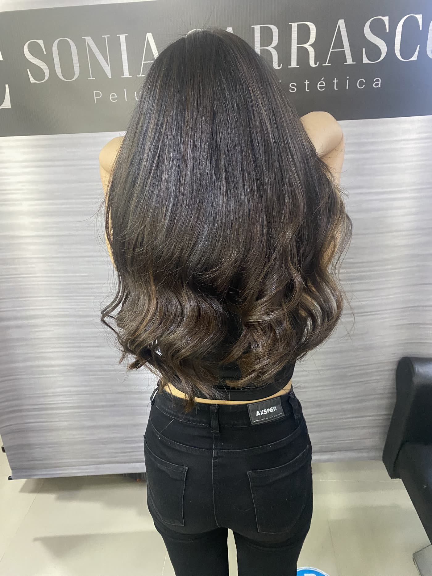Melena castaña con ondas trabajada en el salón, frente al muro de la marca